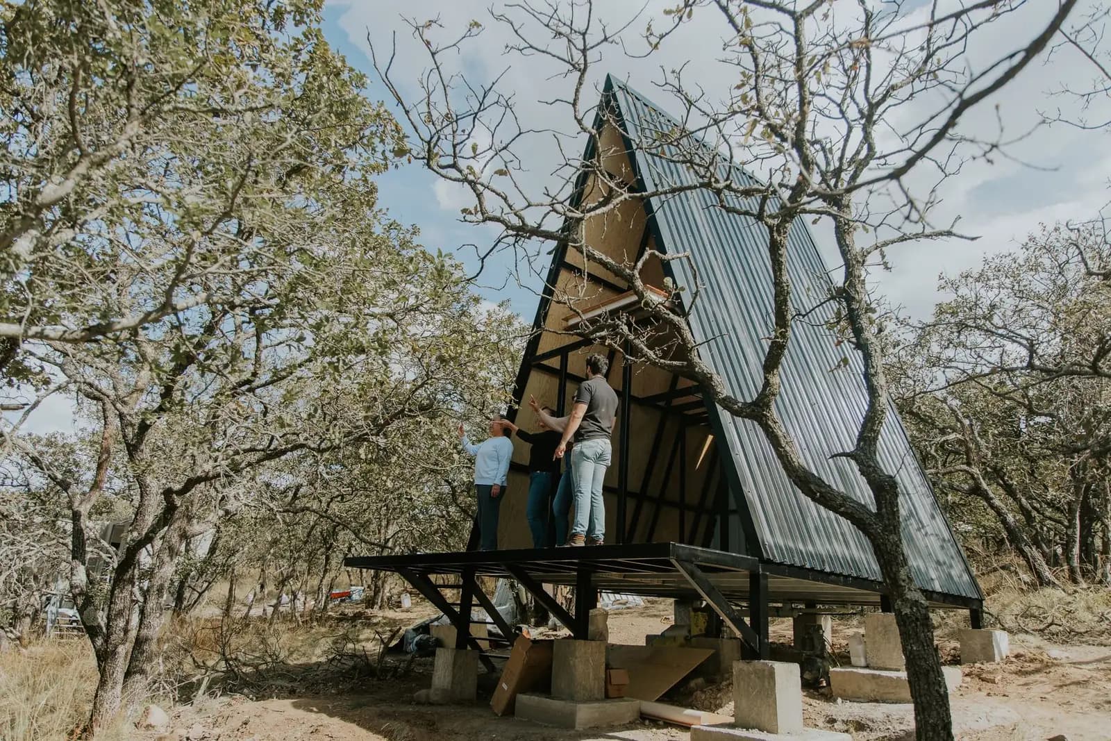 People assembling a compact A-frame home in a wooded setting