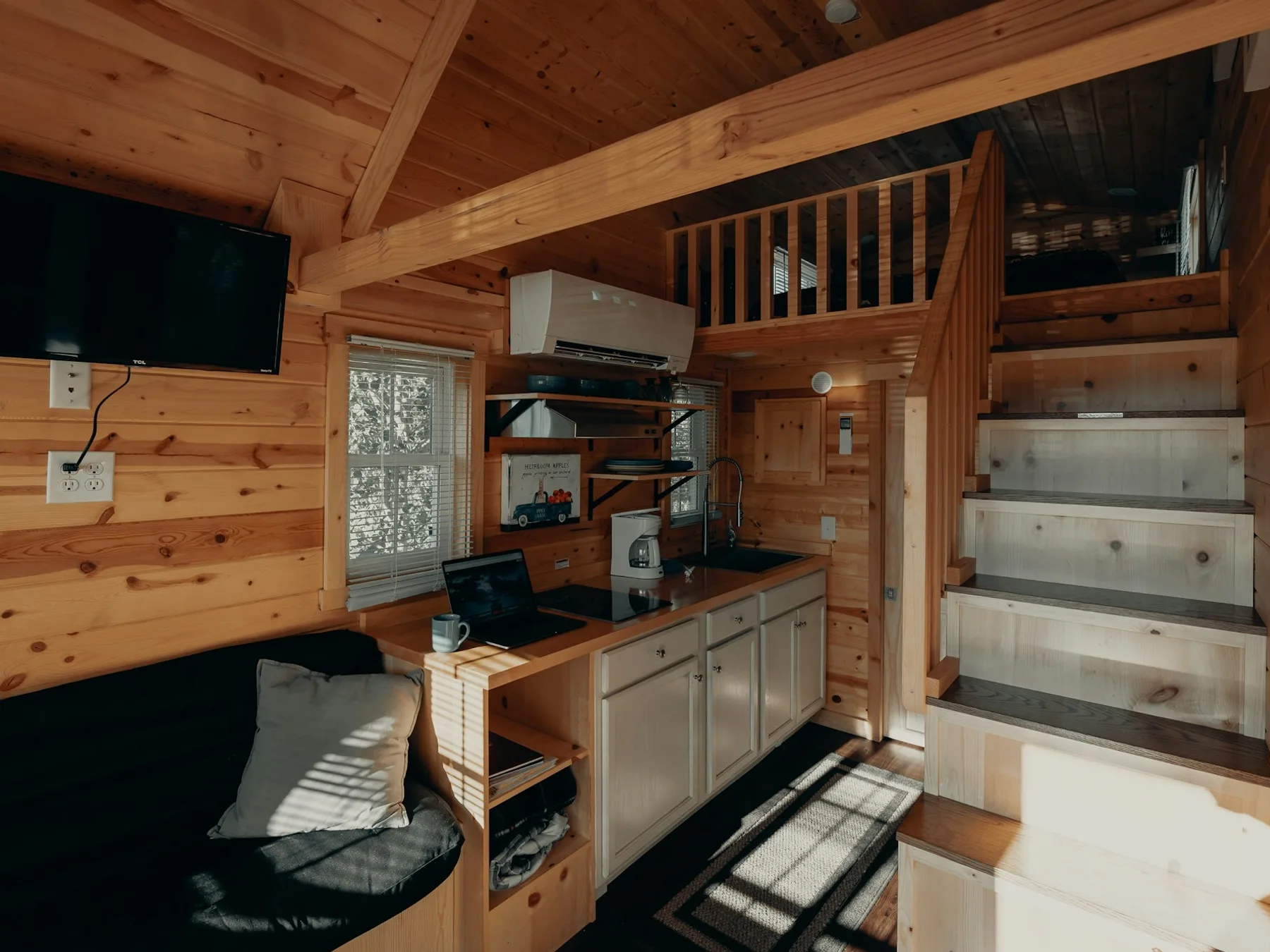 Finished tiny home interior with a wood kitchen, loft stairs, and natural light